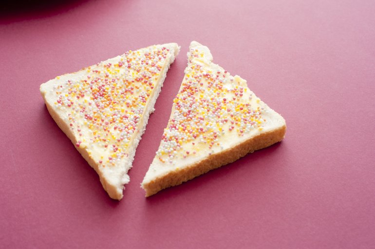 Slice of Australian fairy bread with colorful sprinkles, sugar candy pearls or hundreds and thousands spread over the surface on a red back ground with copy space