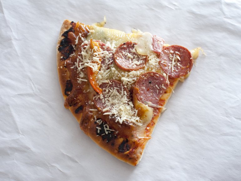 Single slice of traditional Italian pepperoni pizza with cheese topping on crinkled white paper