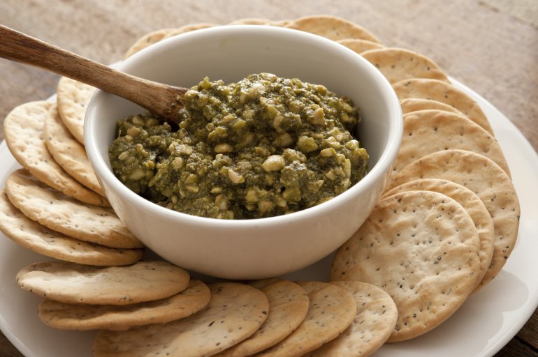 Water biscuits or crackers arranged on a plate around a bowl of pesto nut dip for a tasty healthy snack or appetizer