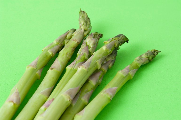 Fresh uncooked green asparagus shoots or spears on a green background