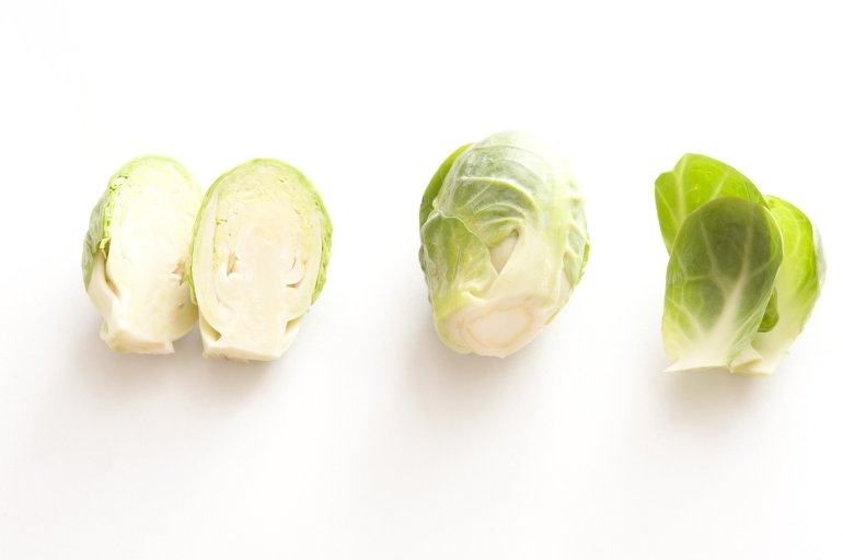 Whole and halved fresh Brussel sprouts Whole and halved fresh Brussel sprouts with loose leaves arranged in a row on white with copy space