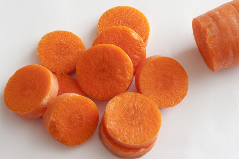 Heap of sliced fresh raw carrot with the tip of the remainder visible alongside ready for use in a salad or cooking, over white
