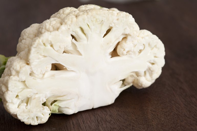 Halved fresh white head of a cauliflower Halved fresh white head of a cauliflower on a dark wooden table with focus to the cross-section