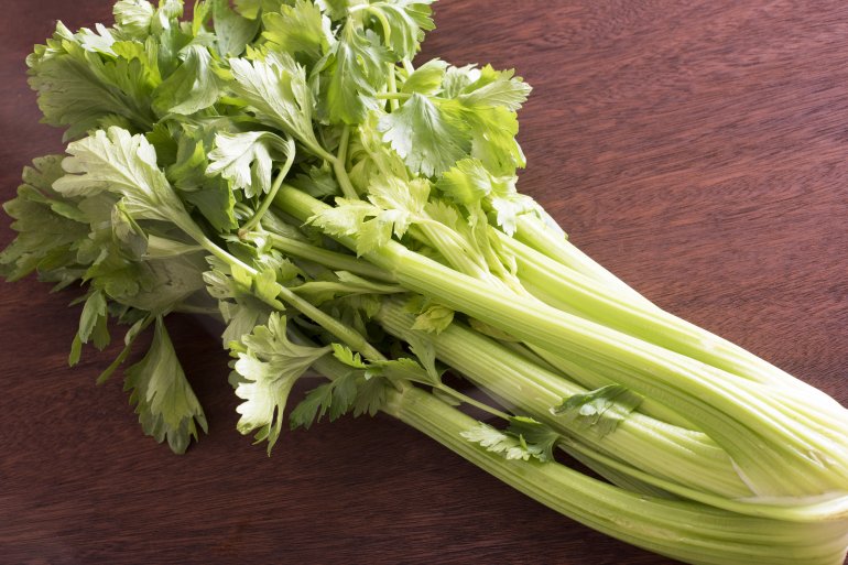 Bunch of fresh green celery stems and leaves Bunch of fresh green celery stems and leaves on a wooden table, a healthy crunchy snack or salad ingredient