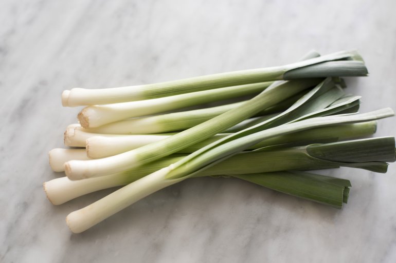 Bunch of fresh leeks in close-up on grey kitchen table surface. Cooking ingredients