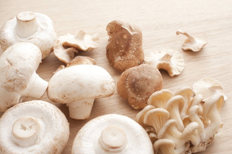 Varieties of fresh edible mushrooms with agaricus bisporus, shitake, and shimeji mushrooms in a random pile on a wooden counter top viewed closeup from above