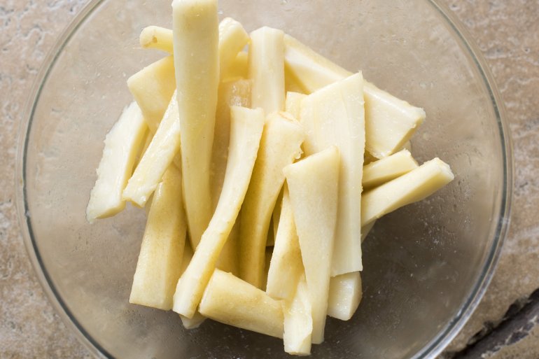 A close up of sliced parsnip wedges in a glass bowl on a kitchen bench.
