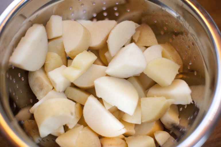 Diced fresh potatoes draining in a metal colander viewed top down close up in a food preparation concept