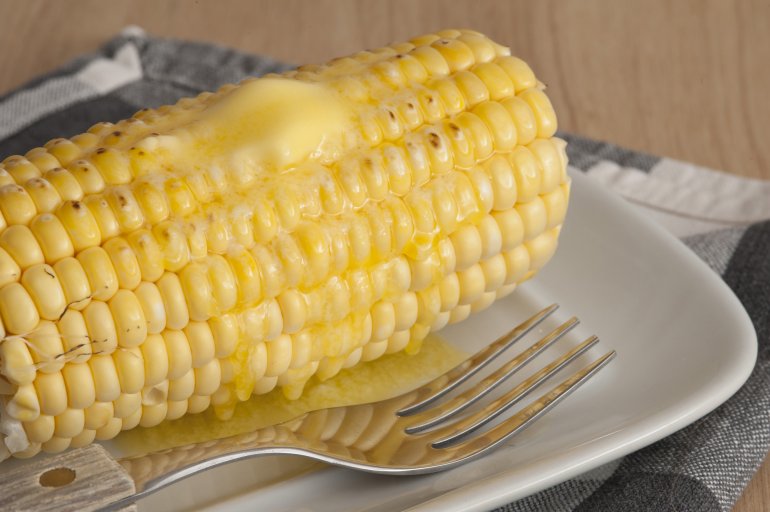 Close-up of cooked corn cob with butter on top served on white plate with fork