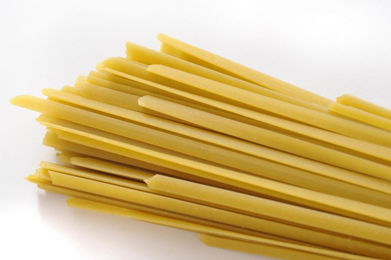 Bundle of traditional dried Italian tagliatelli pasta for use in Mediterranean cuisine on a white background with copyspace