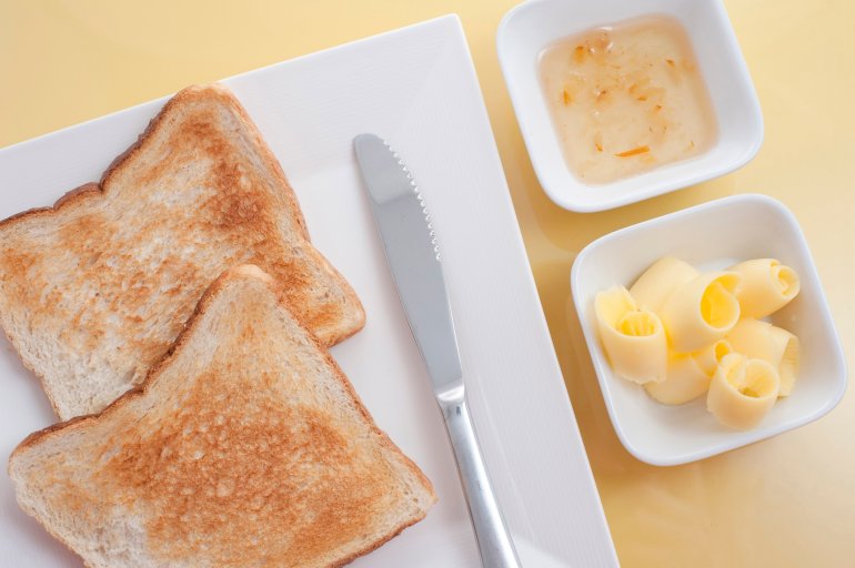 Overhead view of a serving of sliced white toast with butter and marmalade on the side in individual dishes