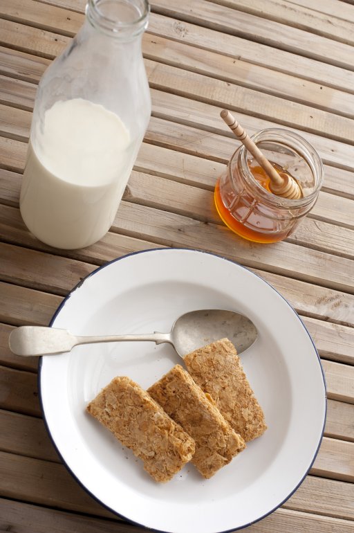 Whole wheat cereal with honey and milk First person perspective view on whole wheat cereal crackers with honey, dipper and large glass jar filled with milk on table with smooth planks of wood