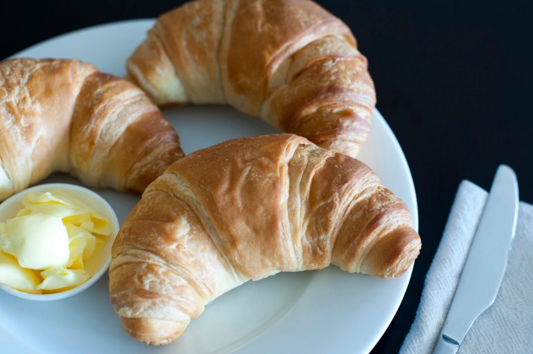 Crisp flaky fresh croissants Overhead view of three golden crisp flaky fresh croissants served with butter on a plate for breakfast