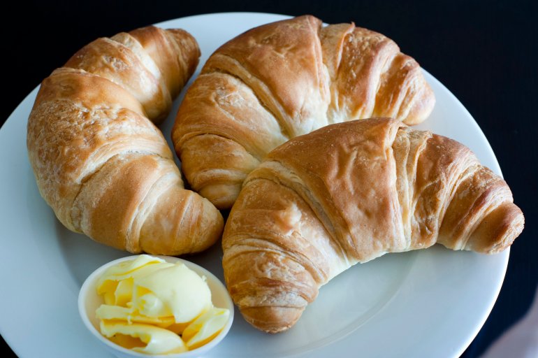 Three flaky golden croissants Three freshly baked flaky golden croissants made with delicious light puff pastry on a plate served with a ramekin of butter for breakfast
