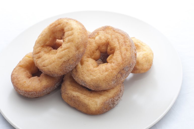 Homemade ring doughnuts made from fried dough served on a white porcelain plate, close up with copy space