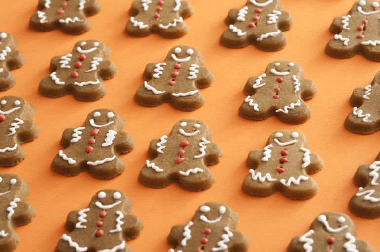 Endless rows of delicious brown icing decorated gingerbread man sweet cookies over orange background