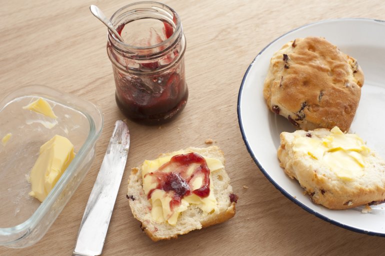 Fresh buttered homemade fruity raisin scones with strawberry jam served on a plate on a wooden table for a tasty snack
