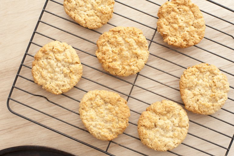 Batch of fresh golden oatmeal cookies cooling on a rack in the kitchen on a wooden counter, overhead view