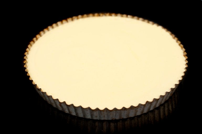 High angle view of a delicious plain baked cheesecake in a round fluted metal oven dish or pie pan on a dark studio background