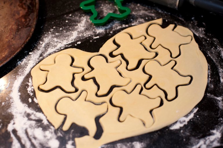 Rolled dough on a kitchen counter with cut out shapes of little figures while baking cookies or biscuits