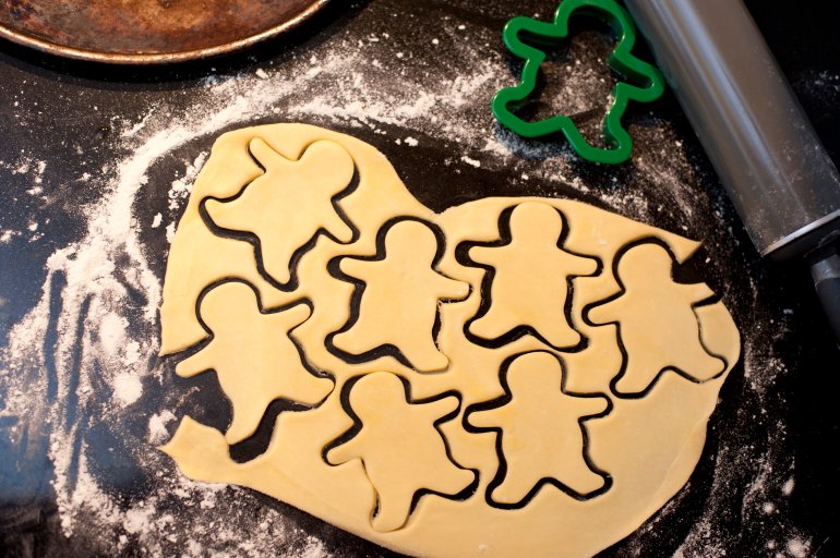 Overhead view of rolled pastry dough with cut out shapes of little figures while cutting cookies for a kids party celebration