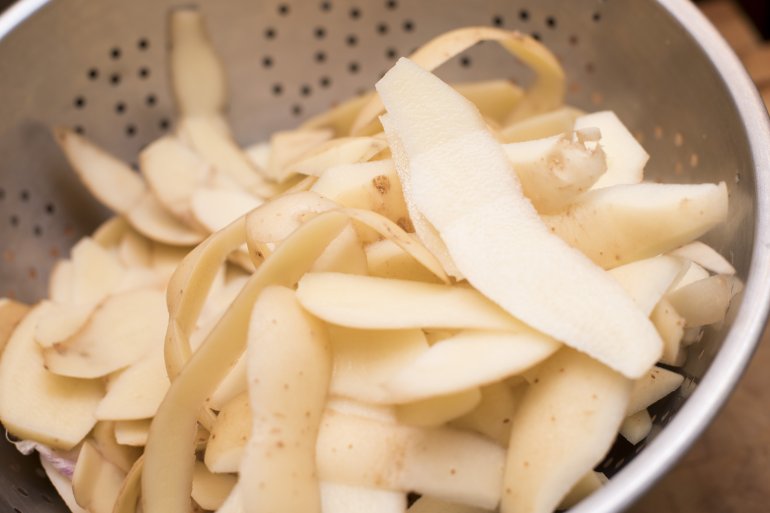 Potato peelings in a metal colander from preparing fresh potatoes for cooking , close up view
