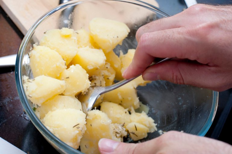 Man preparing parboiled potatoes Man preparing parboiled cleaned and diced potatoes in a glass bowl stirring them with a spoon to season them during cooking