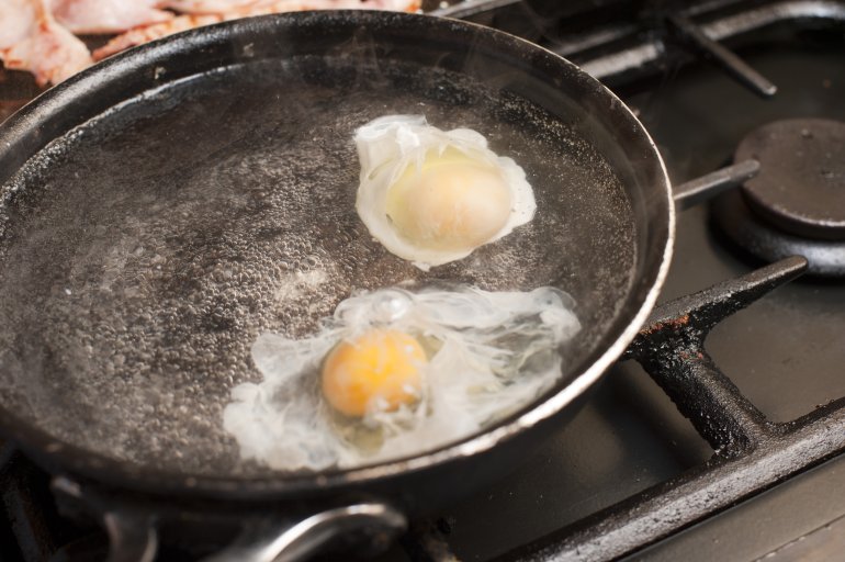 Two eggs being poached in boiling water Two eggs being poached in boiling water on a gas range beside cuts of meat