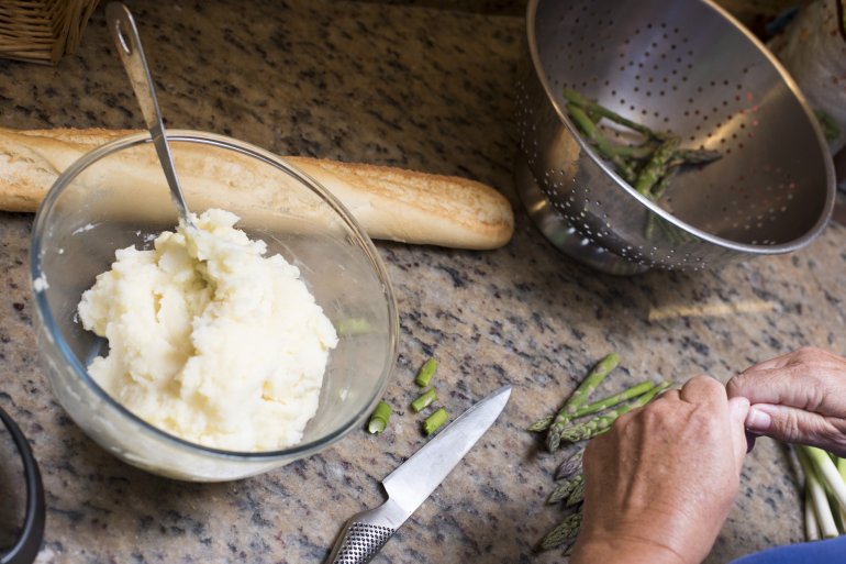 Man preparing the evening meal Man preparing the evening meal with mashed potato and green asparagus tips standing ready as he chops the leeks over a marble kitchen counter