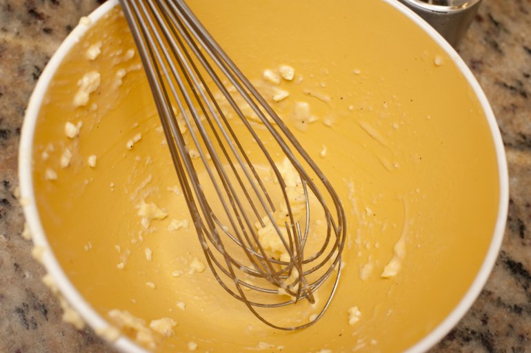 Empty yellow mixing bowl with whisk and batter residue resting on granite counter top