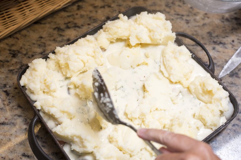 Man preparing a fish pie for dinner Man preparing a fish pie for dinner spooning on the topping before cooking it, close up high angle view