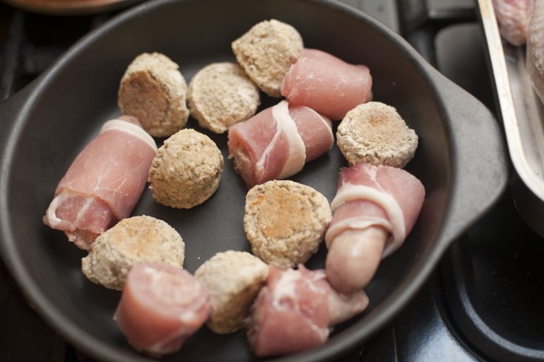 Uncooked bacon rolls standing reading in a pan for cooking with rashers of lean bacon wrapped around sausages, close up high angle view