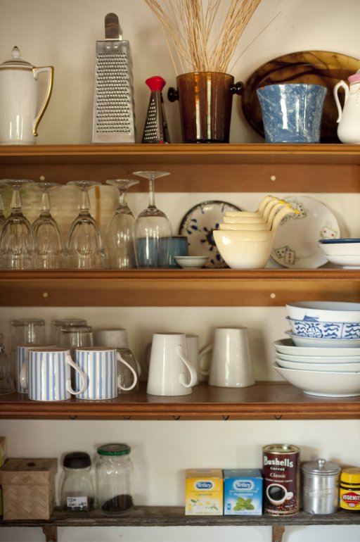 Open storage shelves in a farmhouse kitchen with assorted kitchenware and ingredients mounted onto the wall