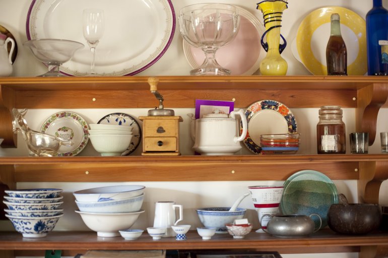 Assorted crockery, utensils and glassware on the shelf of a wooden kitchen dresser in a close up full frame view