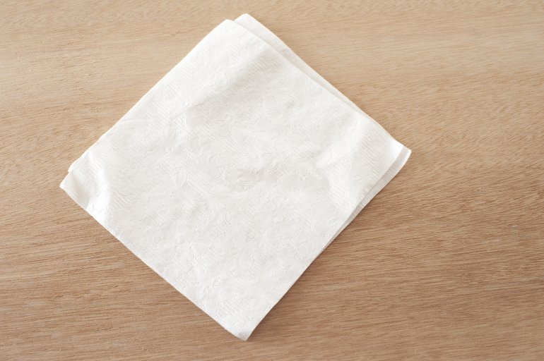 Plain white napkin on a wooden table Plain white napkin centered on a wooden table viewed from above in a conceptual food and catering image