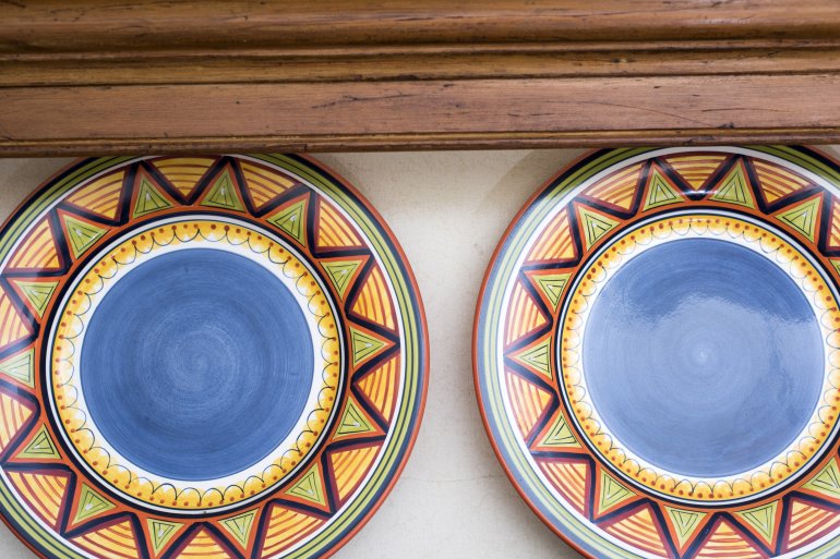 Two colorful patterned plates on a shelf Two colorful patterned pottery plates standing upright for display on a shelf of a wooden kitchen dresser