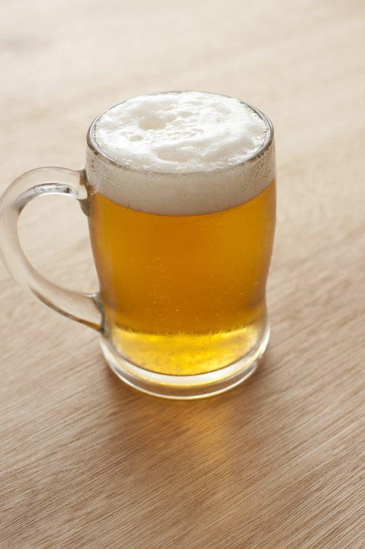 Tankard of beer with a frothy head Tankard of golden draught beer with a frothy head on a wooden table or bar counter, symbolic of the Oktoberfest