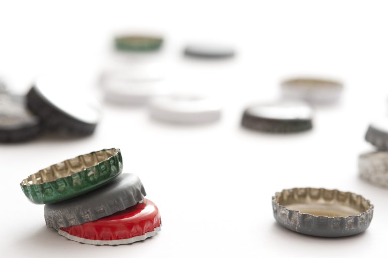 Scattered beer bottle tops randomly placed on a white background viewed low angle with shallow DOF