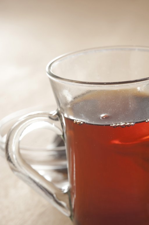 Close up partial view of a clear glass mug with a handle full of strong fresh hot black tea