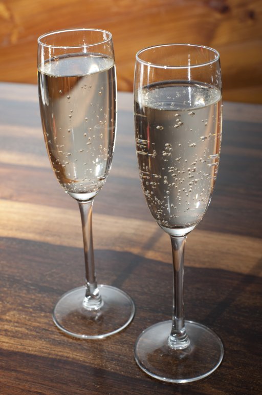 Two full flutes of romantic champagne Two full flutes of champagne or sparkling white wine standing side by side on a wooden counter conceptual of a romantic evening or celebration