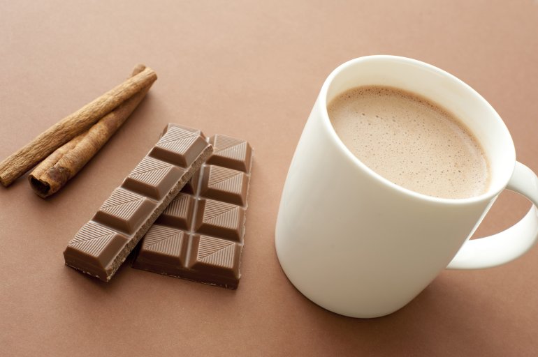 Delicious mug of hot cinnamon chocolate drink for a cold winter day with stick cinnamon and a partial bar of chocolate lying alongside