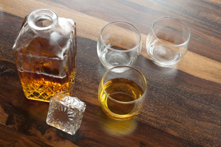 Open whiskey decanter with glasses Open stylish square whiskey decanter with glasses standing on a wooden table or bar counter viewed high angle