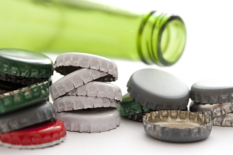 Empty green alcohol bottle with loose caps Empty green alcohol bottle lying on its side surrounded by with old used loose bottle caps on white, close up view