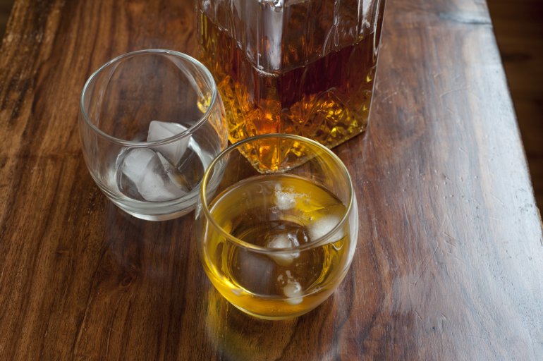 Tumbler of spirits on the rocks with a second empty glass with ice alongside a bottle of alcohol, possibly whiskey, scotch or bourbon