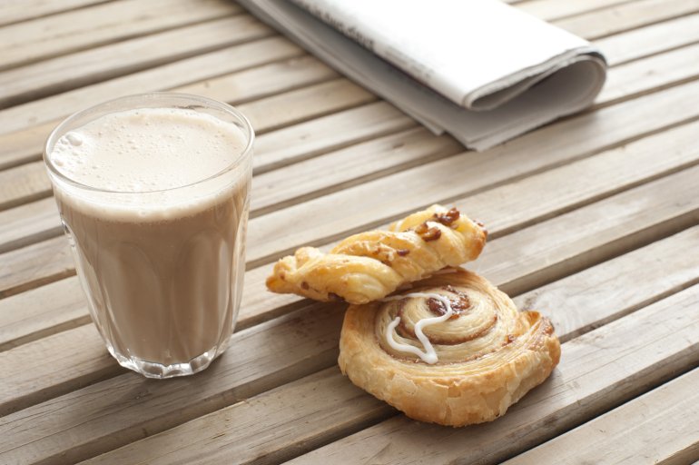 Transparent glass of latte coffee served with freshly baked pastries and a napkin on a wooden slatted table