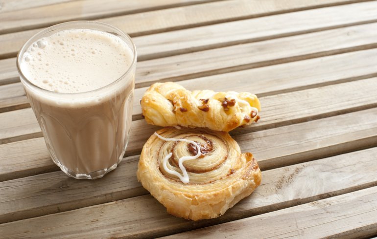 Latte coffee with fresh Danish pastries Latte coffee with fresh apple and cinnamon Danish pastries standing outdoors on a wooden garden table for an early morning snack