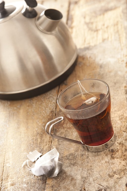 Mug of Tea Brewing on Table Beside Kettle Close Up Still Life of Tea Bag Brewing in Glass Mug on Rustic Wooden Table Beside Metal Kettle