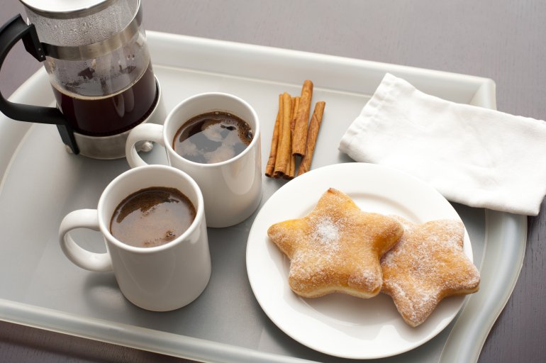 Plunger coffee with two mugs of freshly brewed coffee served on a tray with cinnamon sticks and star-shaped biscuits on a plate