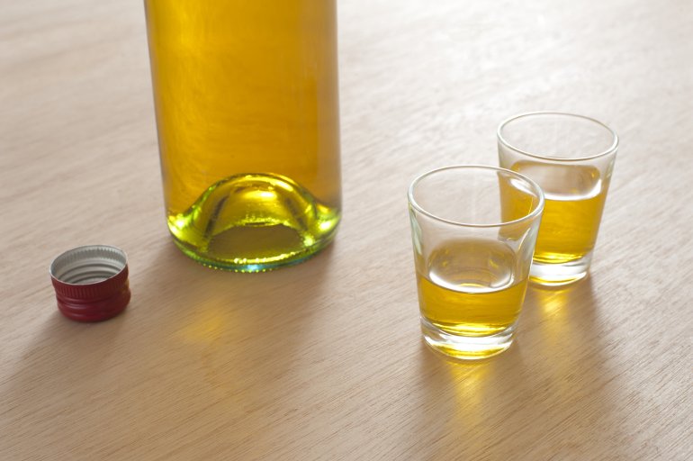 Two full shot glasses with a bottle Two full shot glasses alongside a bottle of spirits, probably either whiskey or brandy, on a wooden bar counter