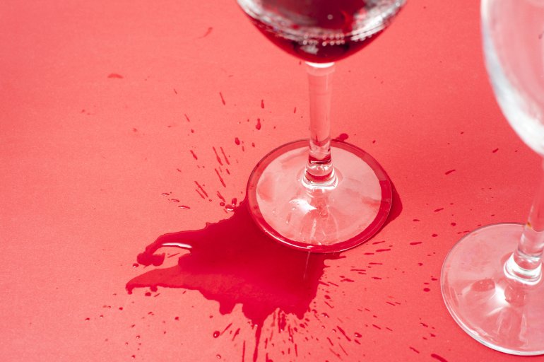 Spilled red wine Spilled red wine splashed around the foot of a wine glass standing on a red background with copyspace